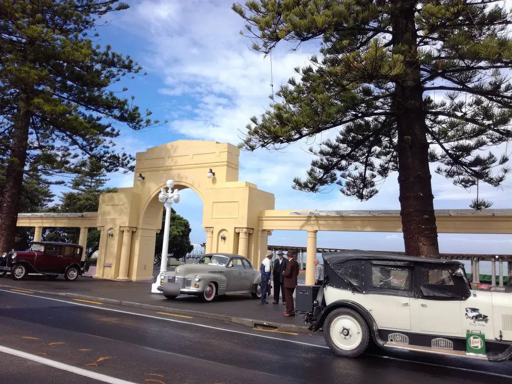 Vintage cars and people in period dress beside the Art Deco arch and colonnade on Marine Parade, Napier