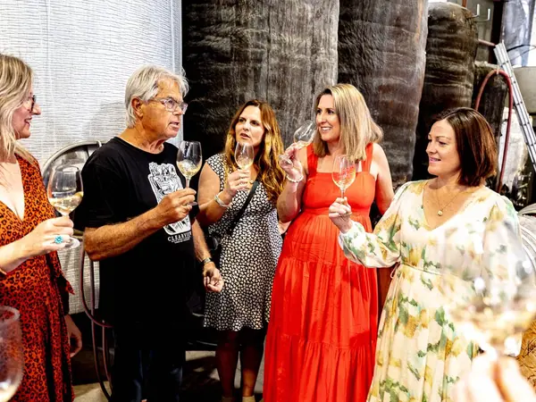 A winemaker hosts guests for a tasting among the barrels