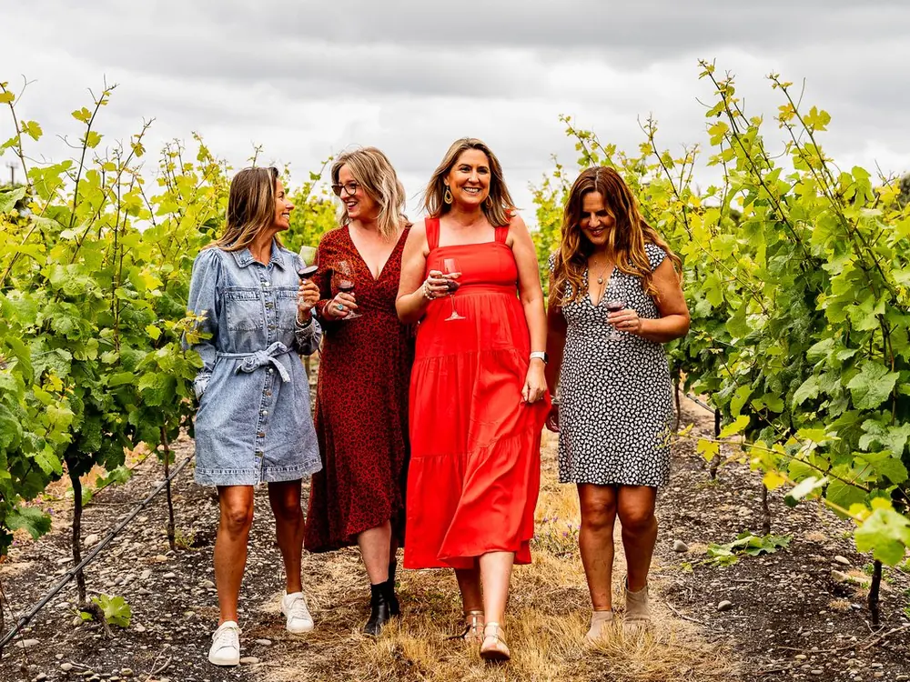 Four guests walking between the vines with glasses of red wine on the Great Wine Capital Signature tour