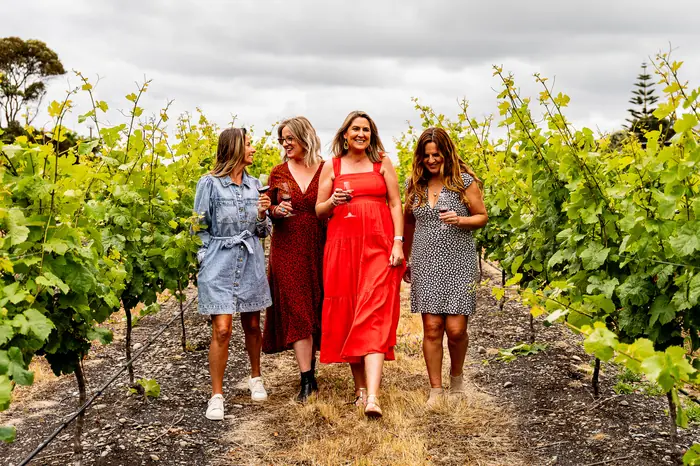 Guests walking between the vines with a glass of red wine on a hosted Hawke's Bay wine tour